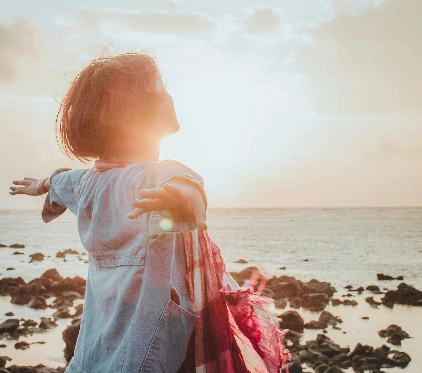 A person stands on a rocky beech with arms outstretched