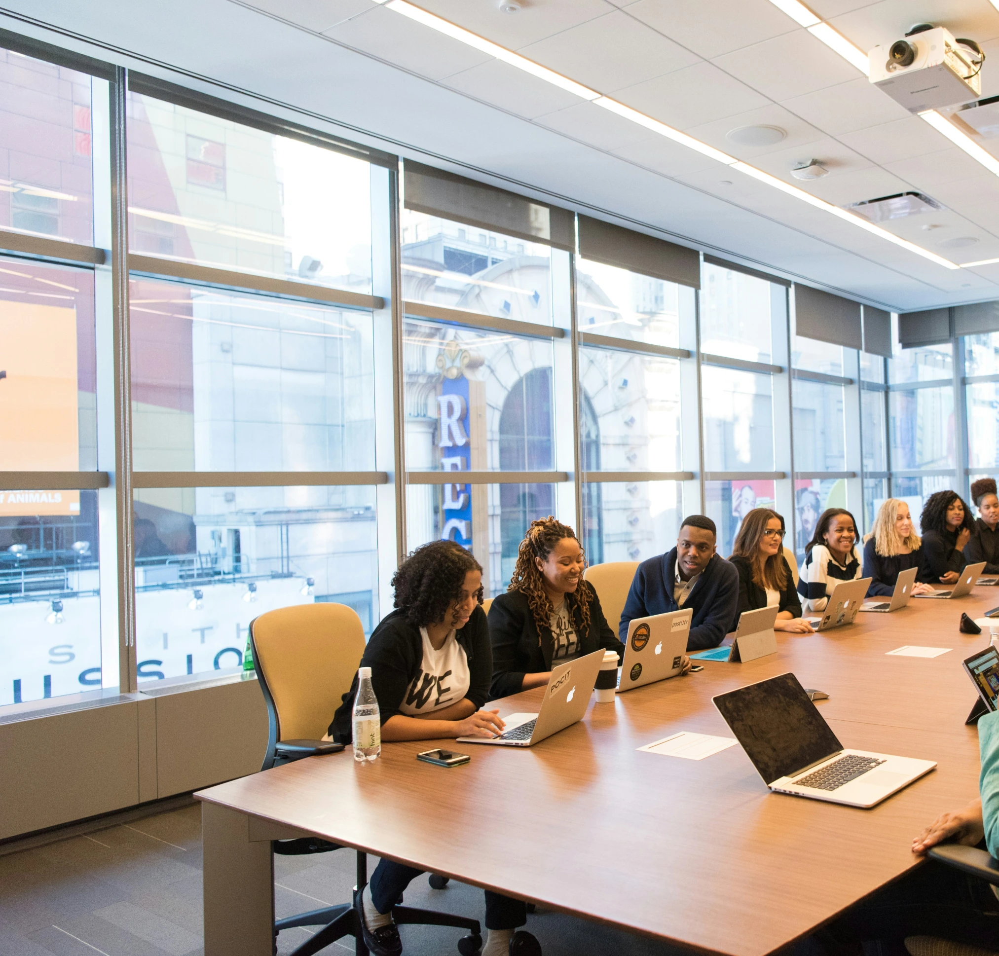 A group of diverse professionals sitting around a conference table with laptops in a bright modern office with a city view